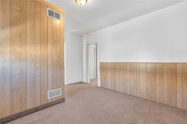 carpeted empty room with visible vents and wood walls