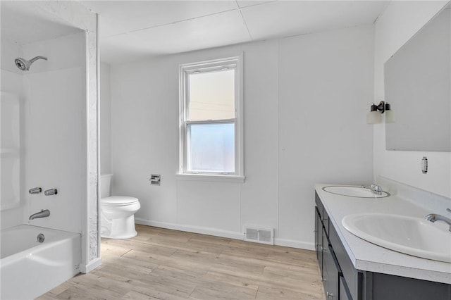 bathroom featuring visible vents, toilet, a sink, wood finished floors, and double vanity