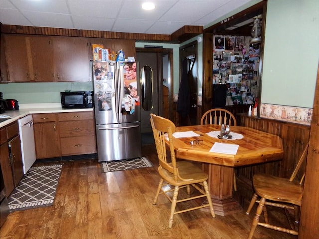 kitchen with wood finished floors, a wainscoted wall, white dishwasher, freestanding refrigerator, and black microwave