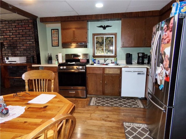 kitchen with under cabinet range hood, appliances with stainless steel finishes, light countertops, and a sink