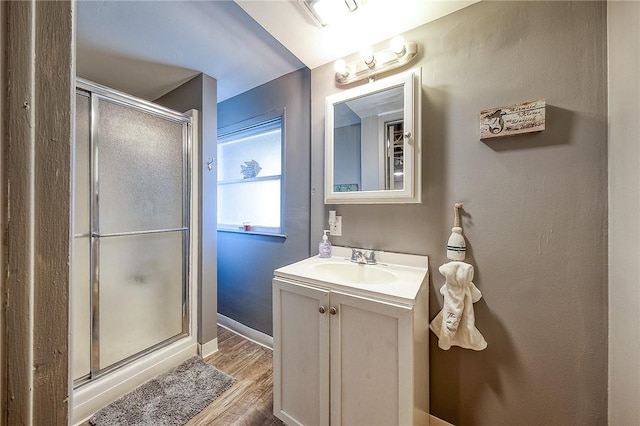 full bath with vanity, wood finished floors, a stall shower, and baseboards