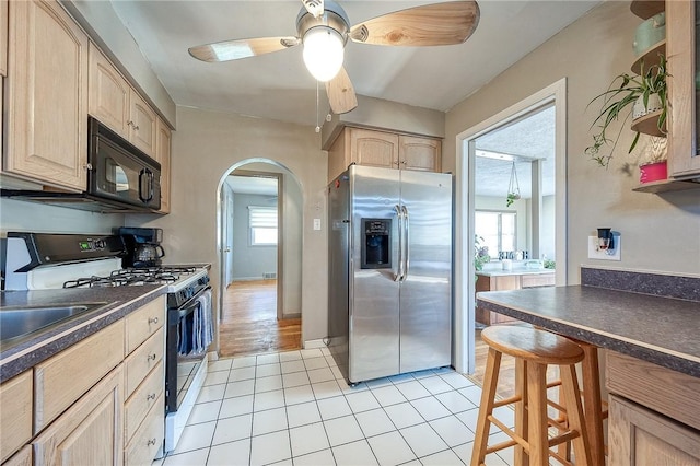 kitchen with light brown cabinetry, dark countertops, range with gas cooktop, stainless steel fridge, and black microwave