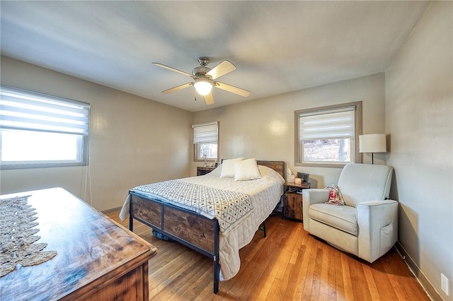 bedroom featuring multiple windows, a ceiling fan, baseboards, and wood-type flooring