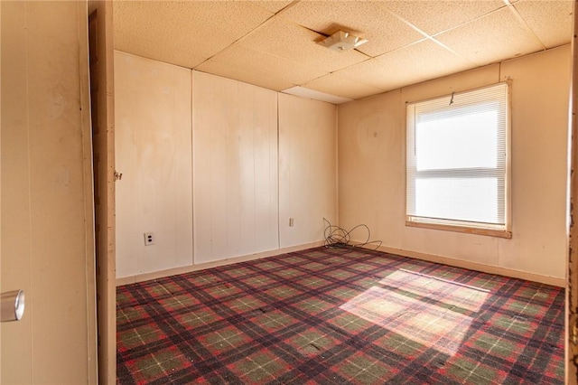 carpeted spare room with a drop ceiling and baseboards