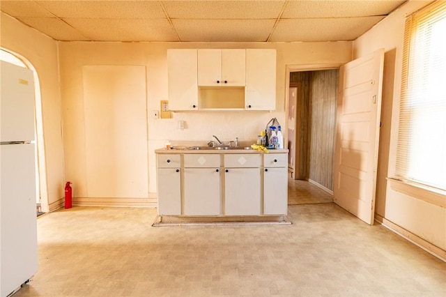 kitchen with a sink, a drop ceiling, white cabinetry, and freestanding refrigerator