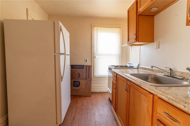 kitchen with wood finished floors, brown cabinetry, freestanding refrigerator, a sink, and range with gas cooktop