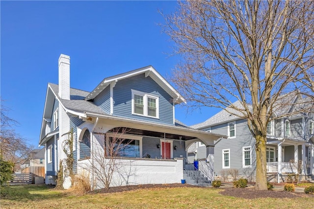 view of front of house featuring covered porch, a chimney, and a front lawn