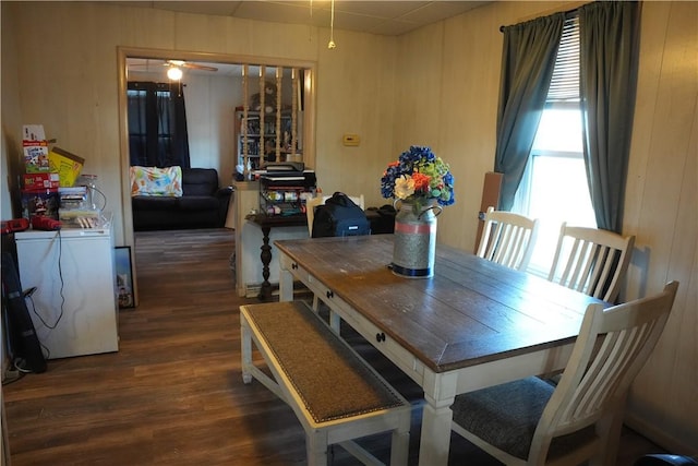 dining space with wood walls, dark wood-type flooring, and ceiling fan