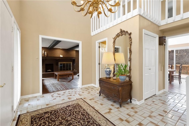 foyer featuring baseboards, a brick fireplace, a chandelier, and a towering ceiling