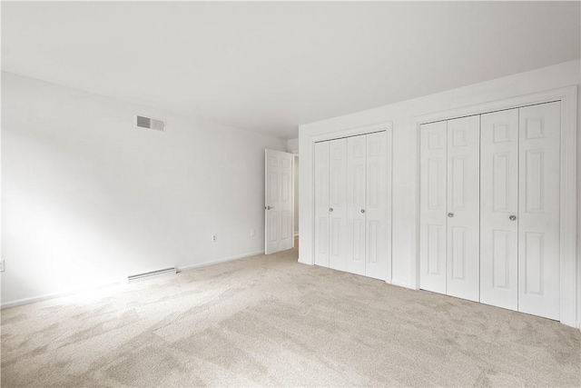 unfurnished bedroom with visible vents, multiple closets, and carpet