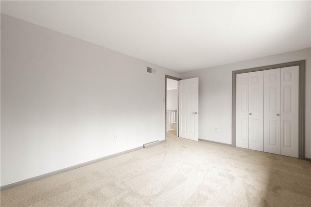 unfurnished bedroom featuring a closet, visible vents, light colored carpet, and baseboards