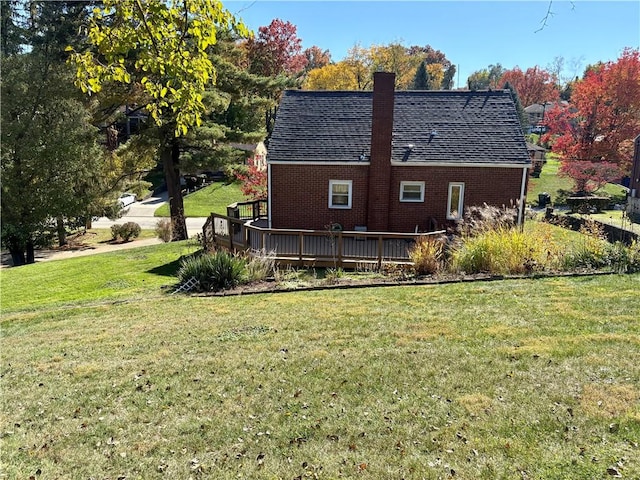 back of property with a lawn, a deck, a shingled roof, brick siding, and a chimney