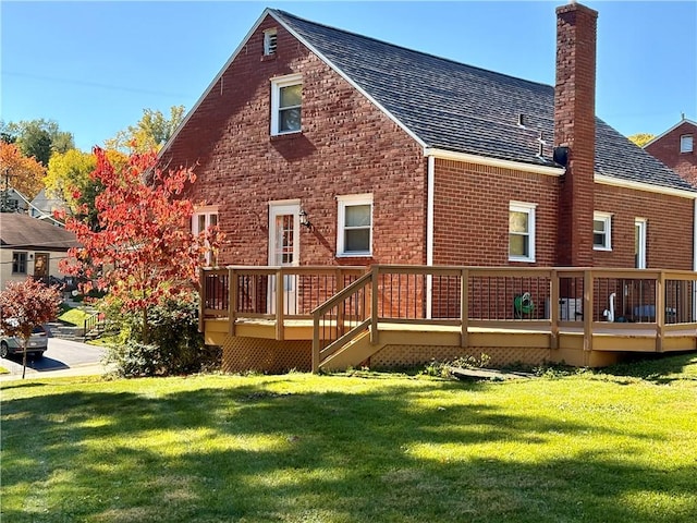 rear view of property featuring a deck, a yard, a shingled roof, brick siding, and a chimney