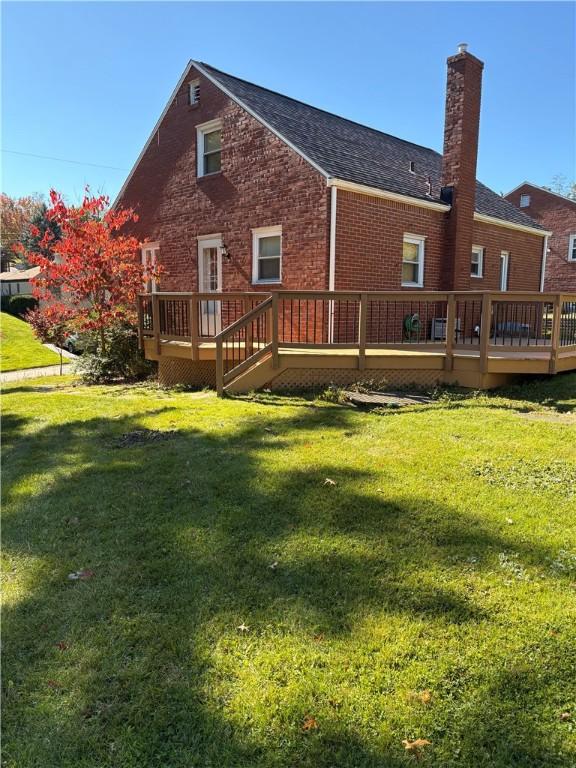 back of house with brick siding, a chimney, a wooden deck, and a yard