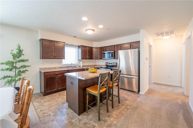 kitchen with visible vents, a sink, stainless steel appliances, a kitchen breakfast bar, and a center island