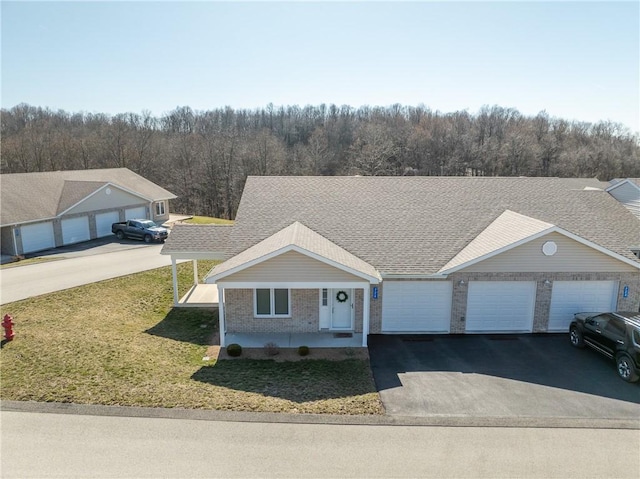 view of front of home with a front yard, a forest view, a shingled roof, a garage, and aphalt driveway