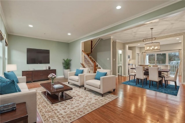 living room with crown molding, a chandelier, stairs, light wood-type flooring, and recessed lighting