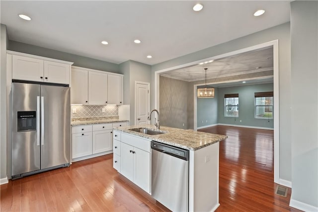 kitchen featuring hardwood / wood-style flooring, a sink, appliances with stainless steel finishes, white cabinets, and decorative backsplash