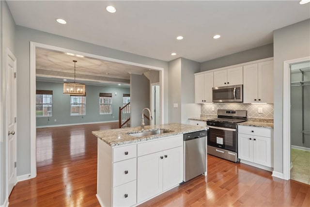 kitchen featuring wood finished floors, an island with sink, a sink, decorative backsplash, and stainless steel appliances