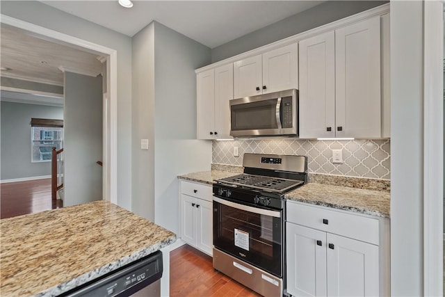 kitchen with light stone countertops, wood finished floors, white cabinets, appliances with stainless steel finishes, and backsplash