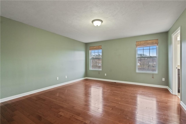 empty room featuring baseboards, wood-type flooring, and a textured ceiling