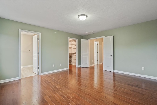 unfurnished bedroom featuring a spacious closet, a textured ceiling, baseboards, and wood finished floors