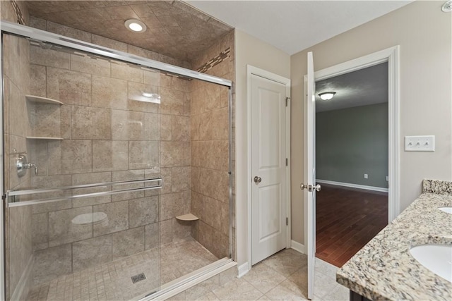 full bath with a shower stall, baseboards, double vanity, tile patterned floors, and a sink