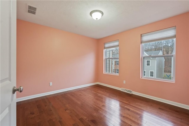 unfurnished room featuring visible vents, dark wood-type flooring, and baseboards