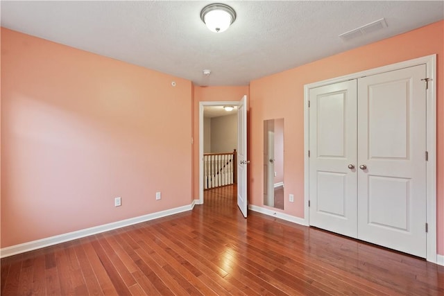 unfurnished bedroom featuring wood finished floors, visible vents, a closet, and baseboards