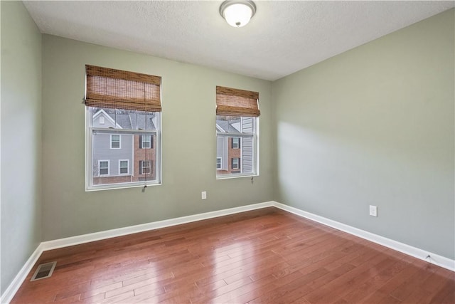 spare room featuring a textured ceiling, wood finished floors, visible vents, and baseboards