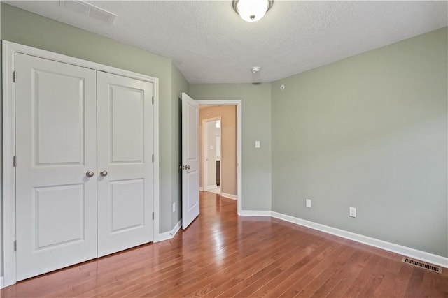 unfurnished bedroom with visible vents, baseboards, a closet, and wood finished floors