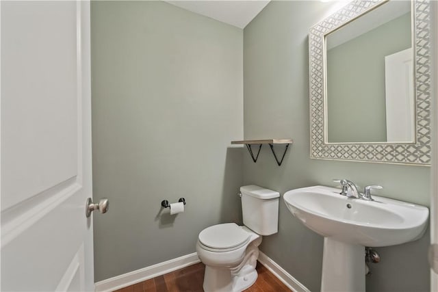 half bathroom featuring toilet, wood finished floors, baseboards, and a sink