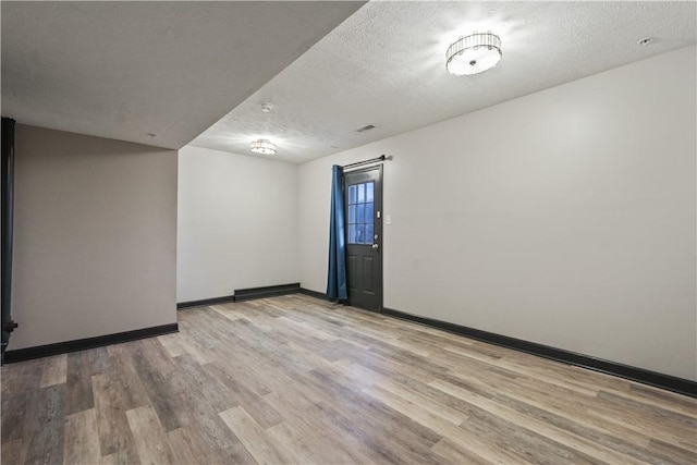 empty room featuring a textured ceiling, baseboards, and wood finished floors