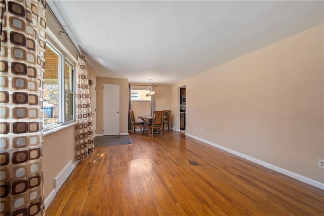 unfurnished living room featuring baseboards, visible vents, wood-type flooring, and a chandelier