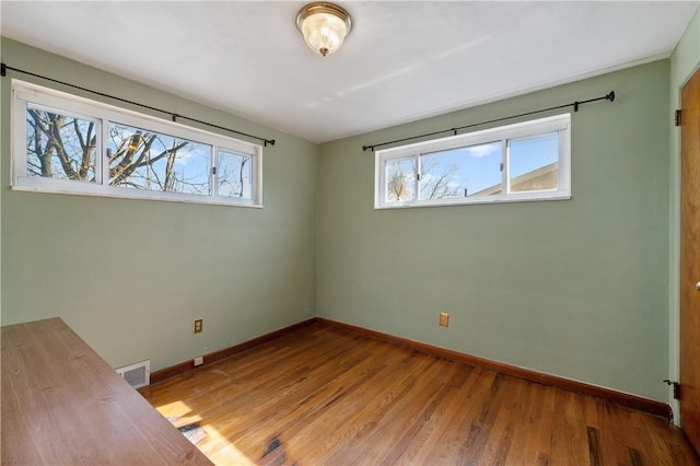 unfurnished bedroom featuring multiple windows, wood finished floors, visible vents, and baseboards