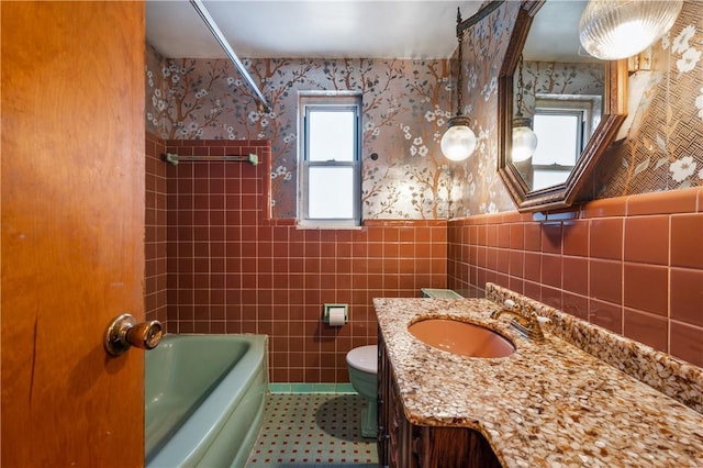 full bath featuring wallpapered walls, tile walls, toilet, wainscoting, and vanity