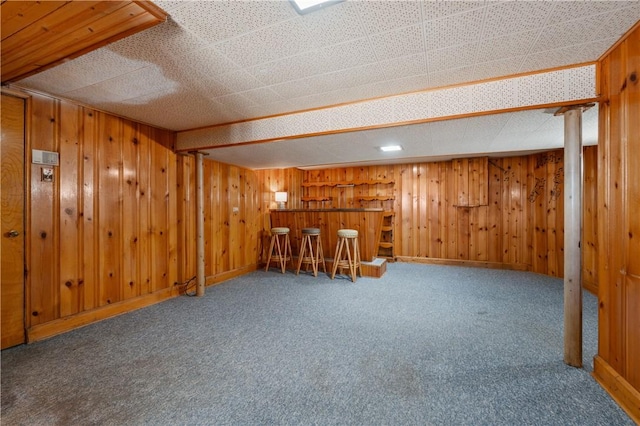 interior space with a bar, wooden walls, carpet, and baseboards