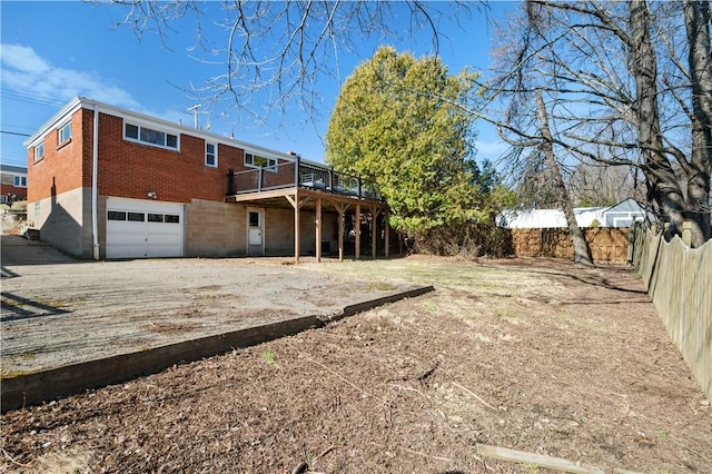 back of house with brick siding, fence, dirt driveway, a deck, and an attached garage