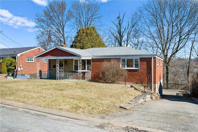 ranch-style house featuring brick siding, aphalt driveway, a porch, a front yard, and a chimney