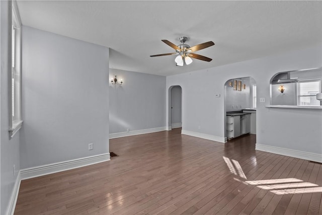 unfurnished living room with arched walkways, baseboards, ceiling fan, and hardwood / wood-style floors