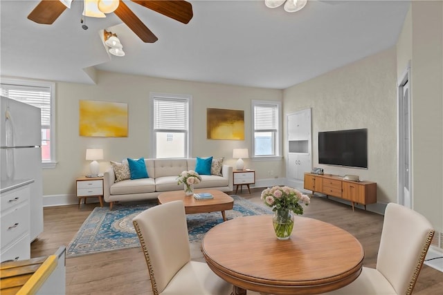 living room featuring baseboards, light wood-style floors, and a ceiling fan