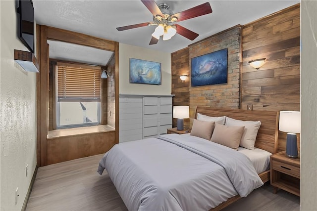 bedroom featuring a ceiling fan, wood finished floors, and wood walls