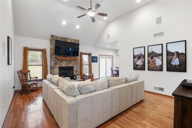 living area featuring a fireplace, visible vents, light wood finished floors, and high vaulted ceiling