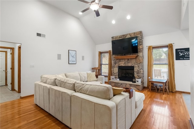 living area with visible vents, high vaulted ceiling, light wood-style flooring, a stone fireplace, and ceiling fan