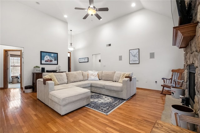 living area featuring visible vents, ceiling fan, light wood-type flooring, a fireplace, and high vaulted ceiling