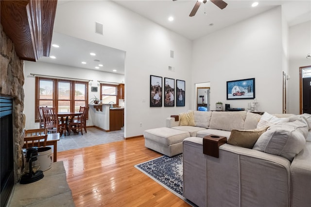 living area featuring ceiling fan, light wood-type flooring, a towering ceiling, and a fireplace