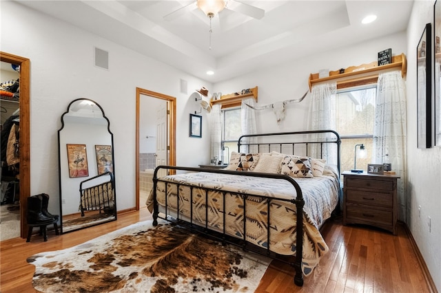 bedroom with hardwood / wood-style floors, a tray ceiling, multiple windows, and visible vents