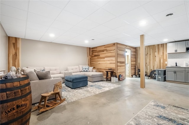 living area with wooden walls, a drop ceiling, visible vents, and concrete flooring