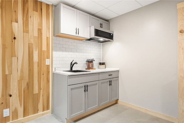 kitchen with gray cabinets, a sink, stainless steel microwave, decorative backsplash, and a paneled ceiling