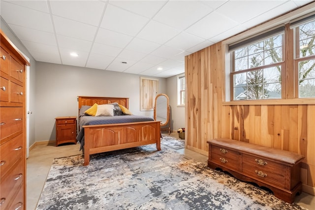 bedroom with a drop ceiling, baseboards, and wooden walls